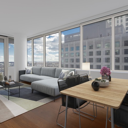 Living and dining area with a table for four, sectional couch and area rug with large windows